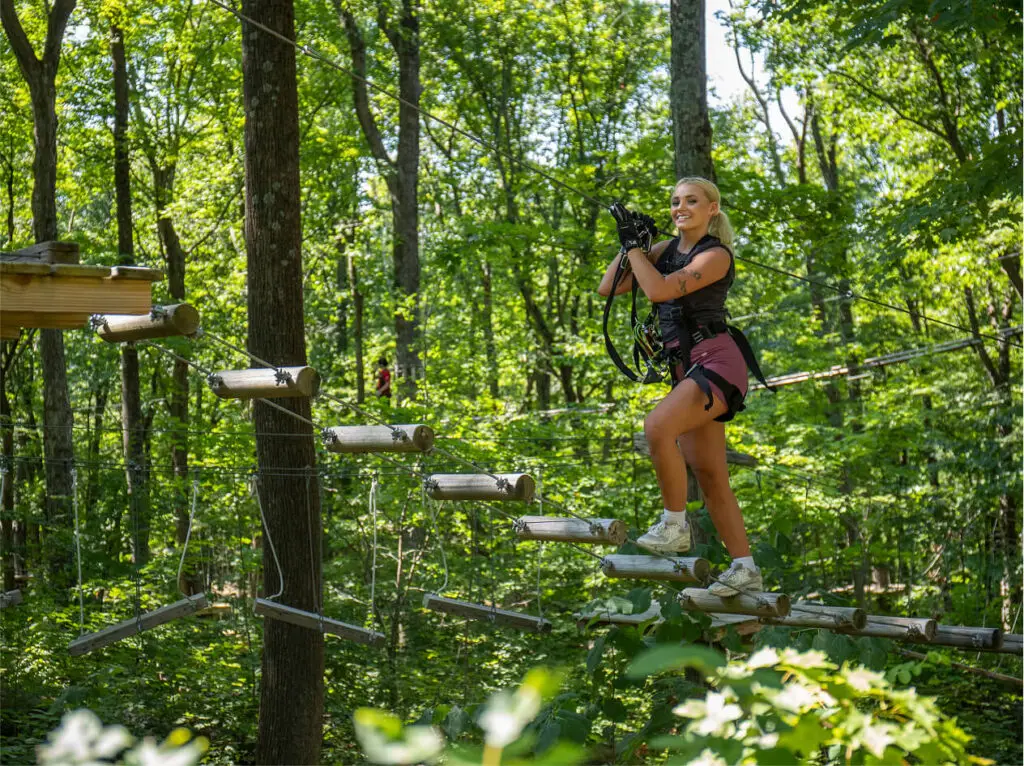 Young smiling woman navigating an aerial rope course at TreEscape Aerial Adventure Park at The Great Gorge, suspended mid-air among the trees.