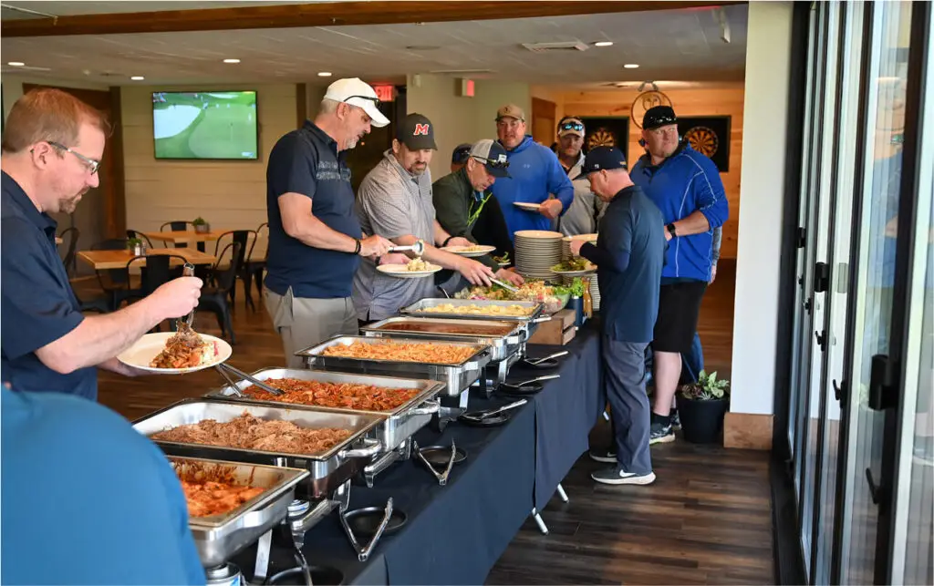 Group of men relaxing after a round of golf at The Great Gorge in Vernon, NJ, enjoying a BBQ selection, with the golf course in the background and a laid-back atmosphere.