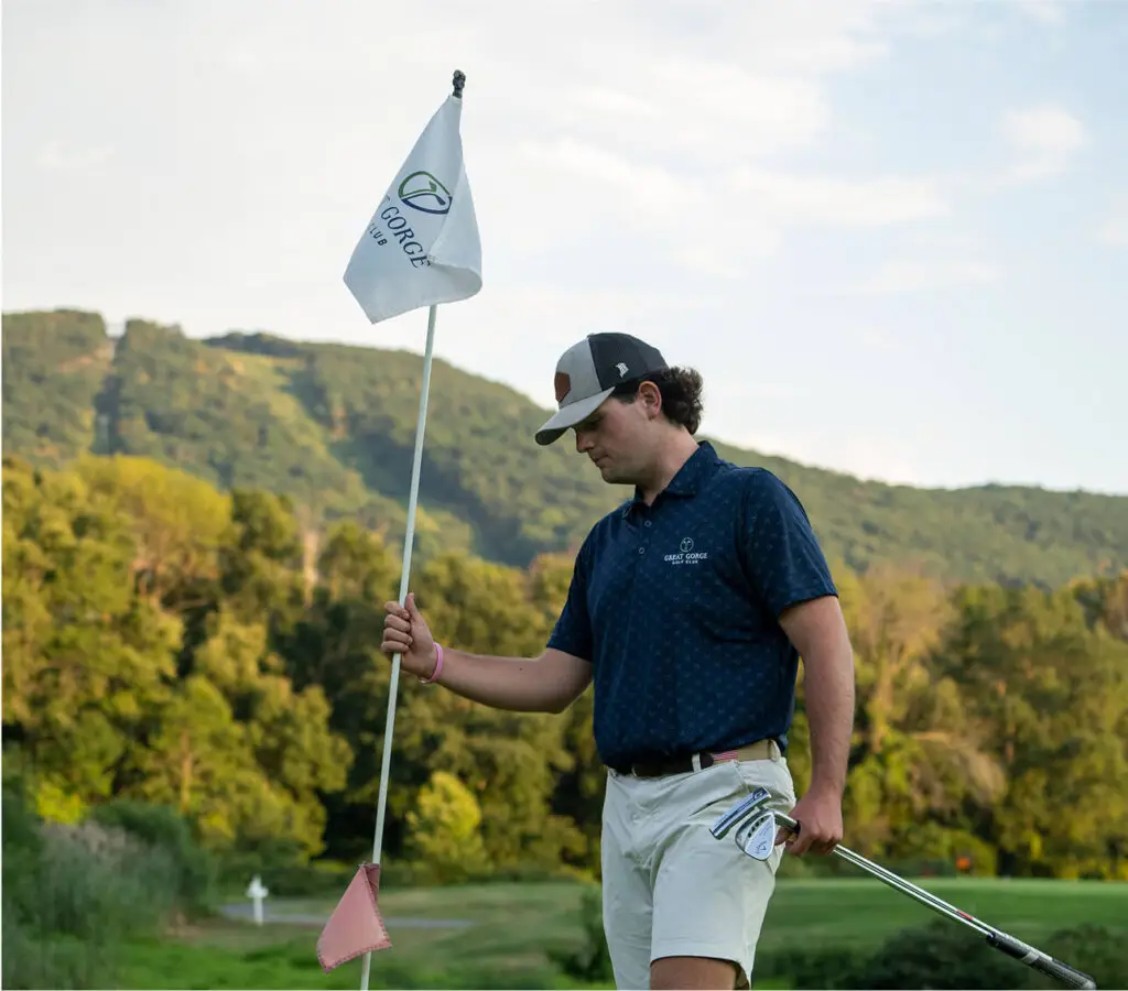 Golfer standing next to a flag with The Great Gorge logo and name displayed, ready to take a shot on the course, with lush fairways and scenic views in the background. Symbol of latest golf stats