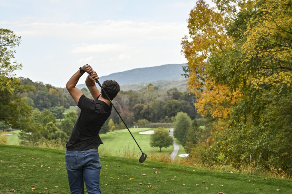 Young man preparing to hit a golf ball at Great Gorge Golf Club on a crisp fall day, surrounded by colorful autumn foliage. Symbol of hole-in-one stats
