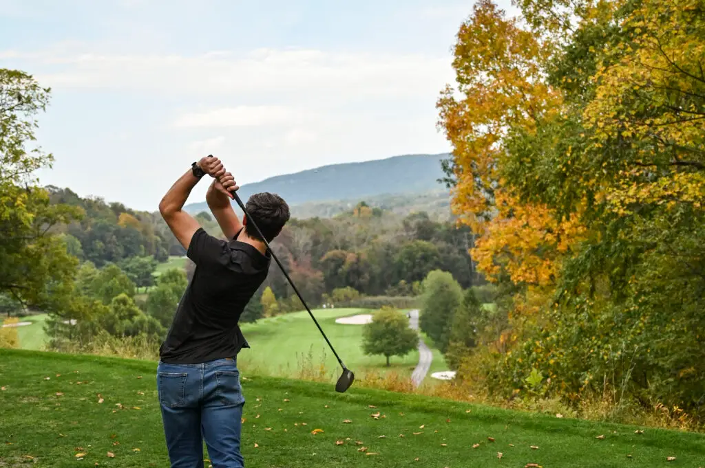 Young man preparing to hit a golf ball at Great Gorge Golf Club on a crisp fall day, surrounded by colorful autumn foliage. Symbol of hole-in-one stats